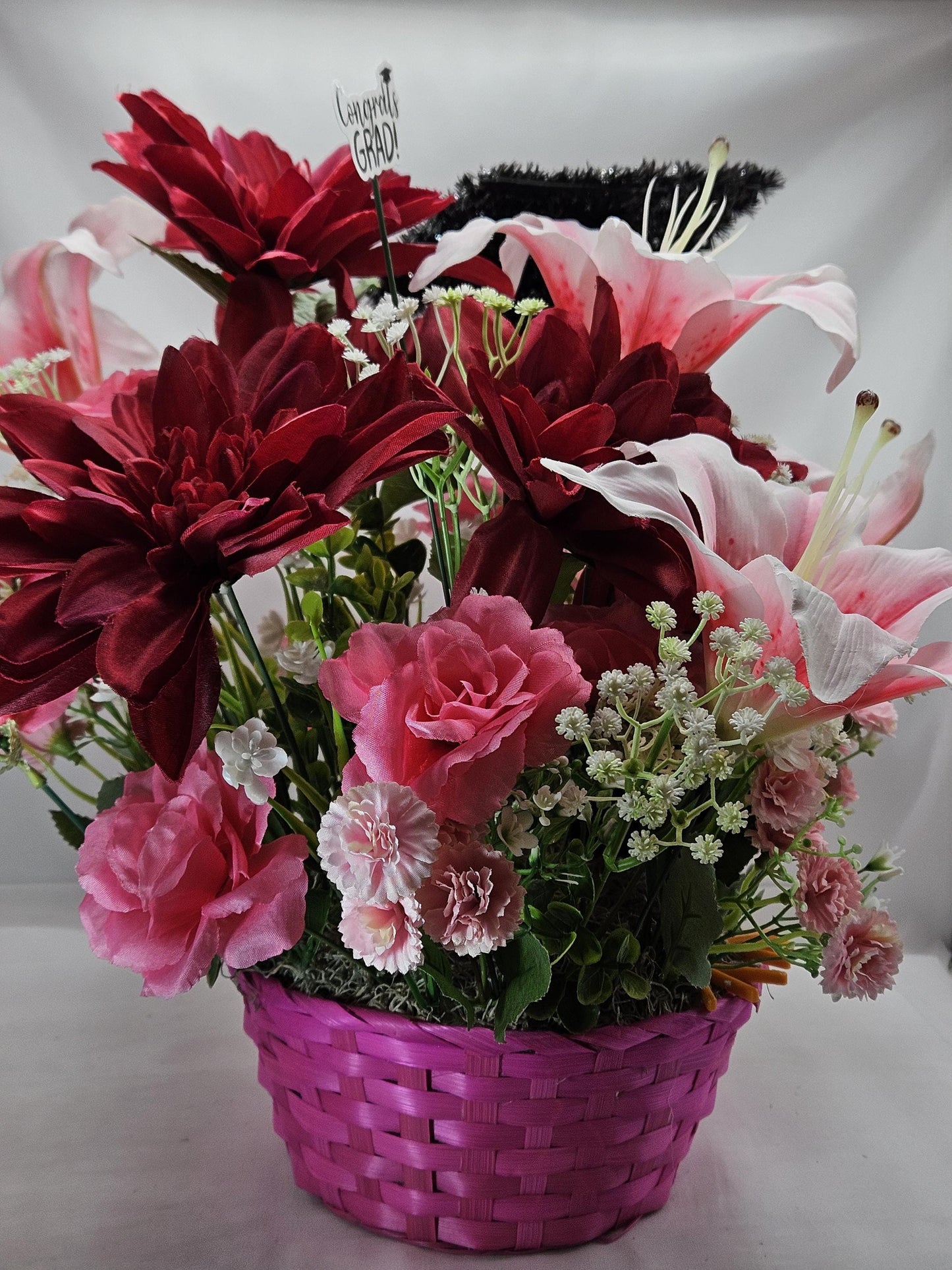 Celebrate The Graduate W/Pink Wicker Basket of Flowers/Greenery/A Sparkly Graduation Hat/A Graduate Bird In Front/Congratulations Messa