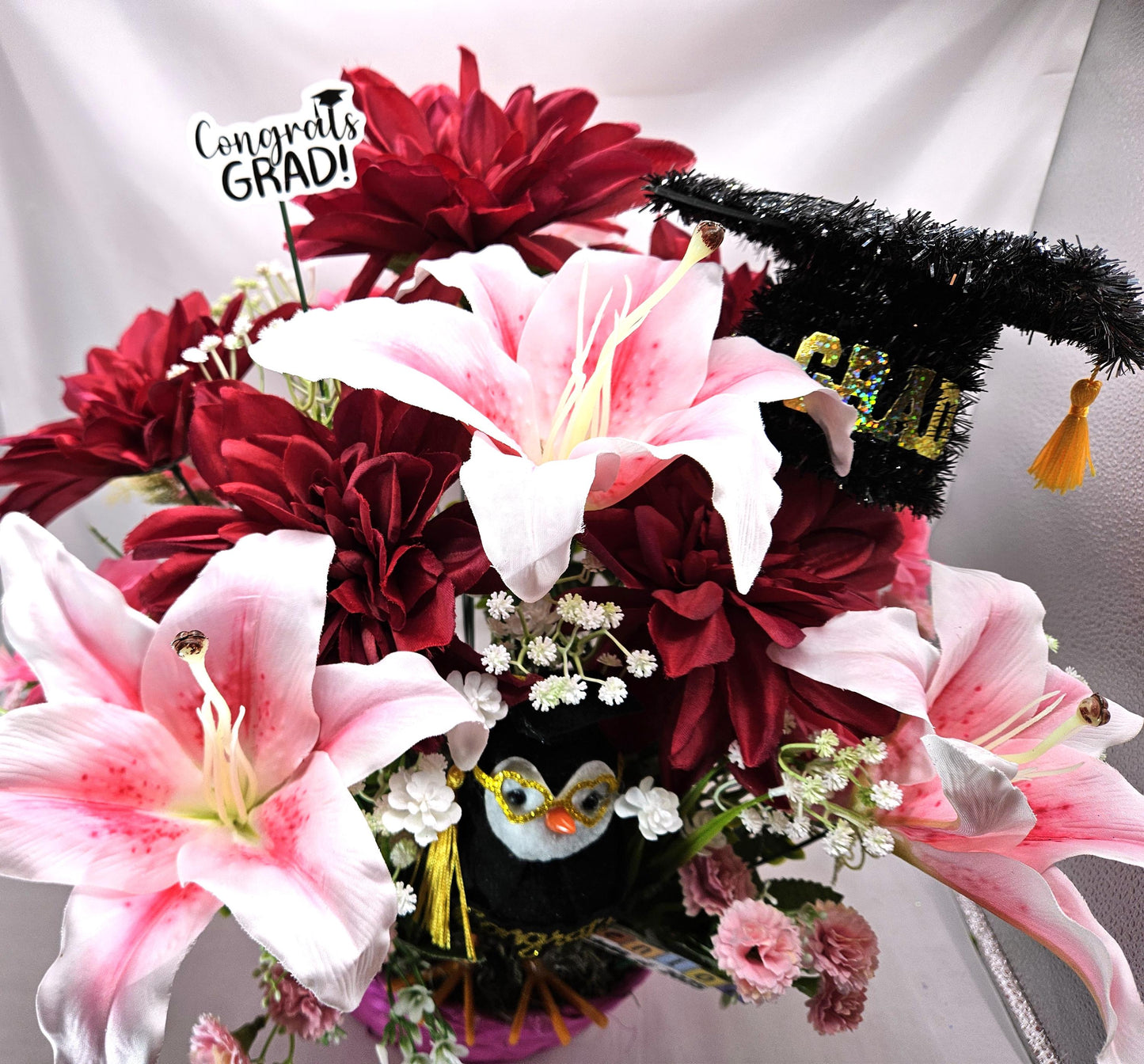 Celebrate The Graduate W/Pink Wicker Basket of Flowers/Greenery/A Sparkly Graduation Hat/A Graduate Bird In Front/Congratulations Messa