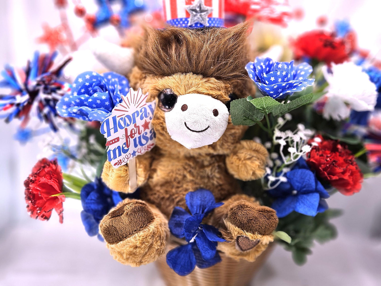 Stuffed Patriotic Steer Celebrating the USA within a Garden of Red/White/Blue Roses/Carnations/Greenery/Sparkly Stars/Other Glitter Accents