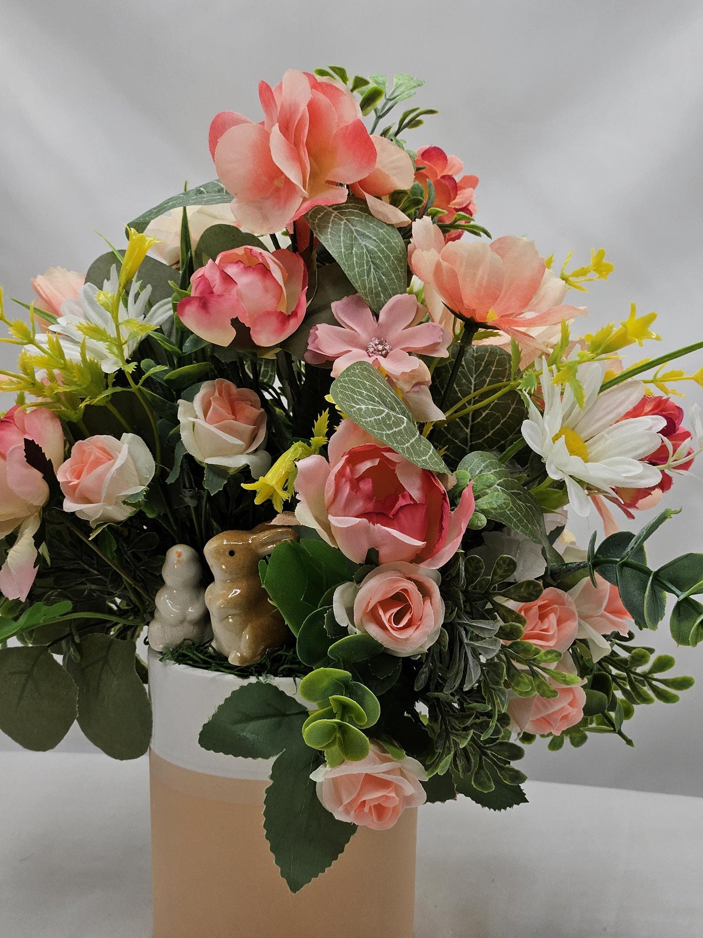 Ceramic Bunnies in a Pink/Peach/Yellow Flower Garden, Lush Greens and Baby's Breath, All Nestled in a Two Tone Ceramic Beige/White Vase