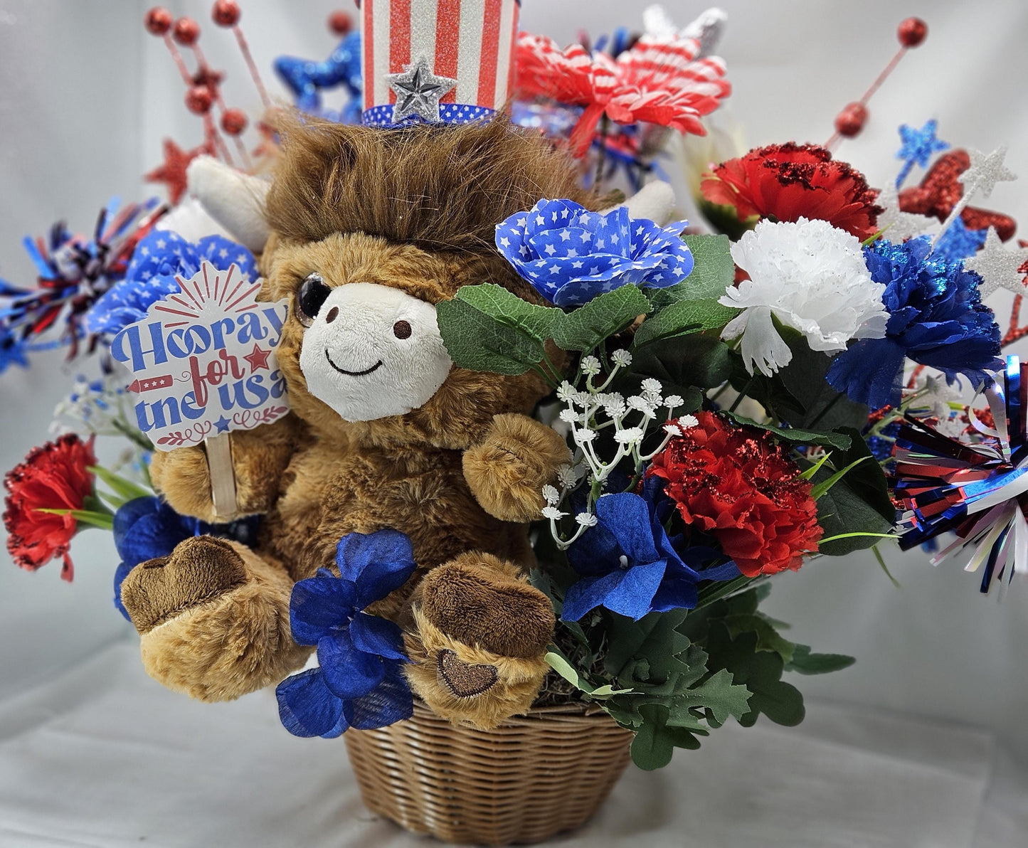 Stuffed Patriotic Steer Celebrating the USA within a Garden of Red/White/Blue Roses/Carnations/Greenery/Sparkly Stars/Other Glitter Accents