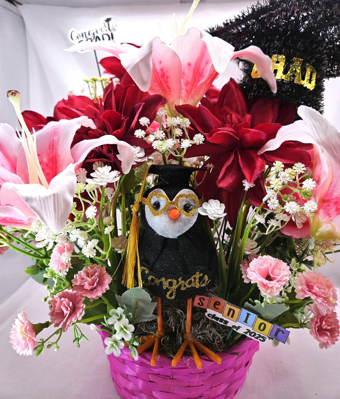 Celebrate The Graduate W/Pink Wicker Basket of Flowers/Greenery/A Sparkly Graduation Hat/A Graduate Bird In Front/Congratulations Messa