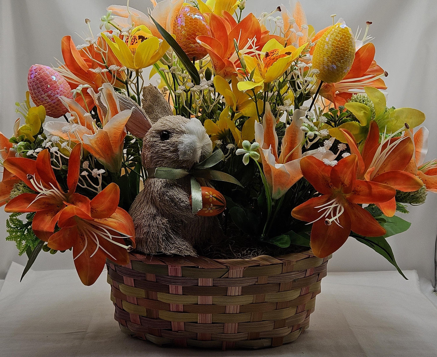 Rattan Easter Bunny in a Multi-colored Basket, Surrounded by Lush and Lovely Lilies, Greens, Baby's Breath,Orange and Yellow Hues