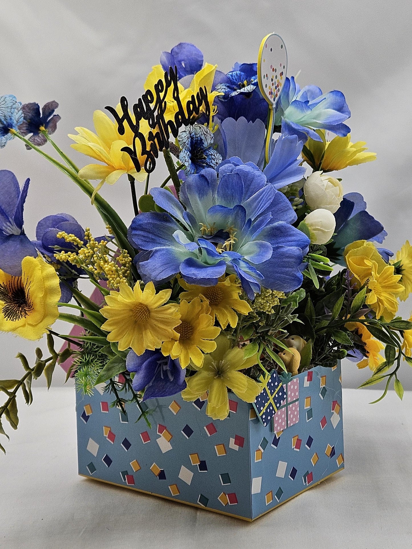 Birthday Flower Arrangement set in Blue Gift Box, Glittery BD Cake on the Lid, Lovely Blue/Yellow Blooms, Cute Bunnies, Baloons, Gifts