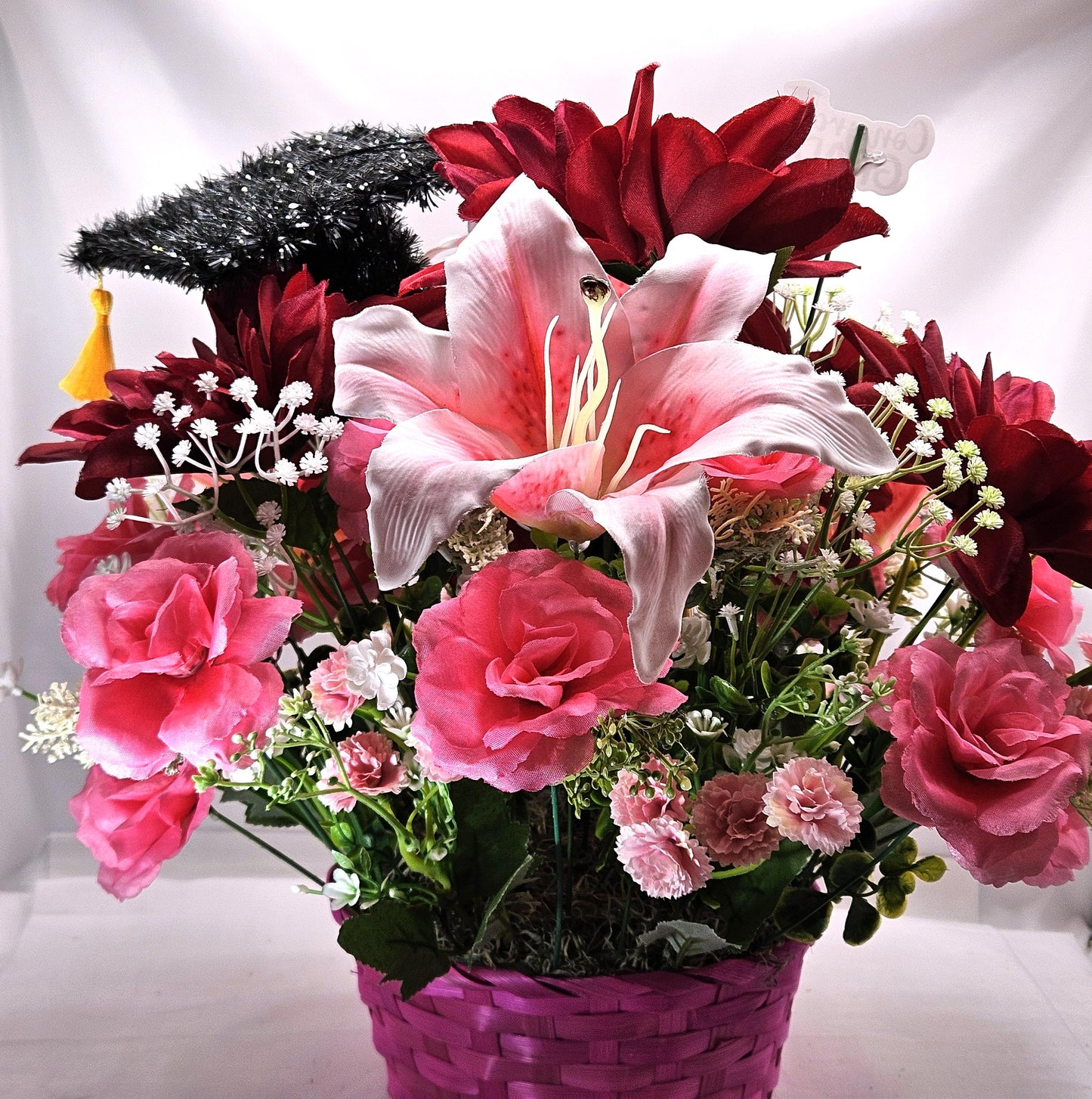 Celebrate The Graduate W/Pink Wicker Basket of Flowers/Greenery/A Sparkly Graduation Hat/A Graduate Bird In Front/Congratulations Messa