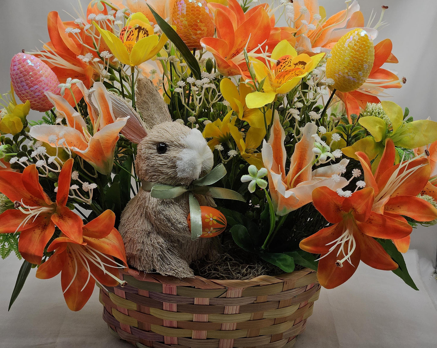 Rattan Easter Bunny in a Multi-colored Basket, Surrounded by Lush and Lovely Lilies, Greens, Baby's Breath,Orange and Yellow Hues