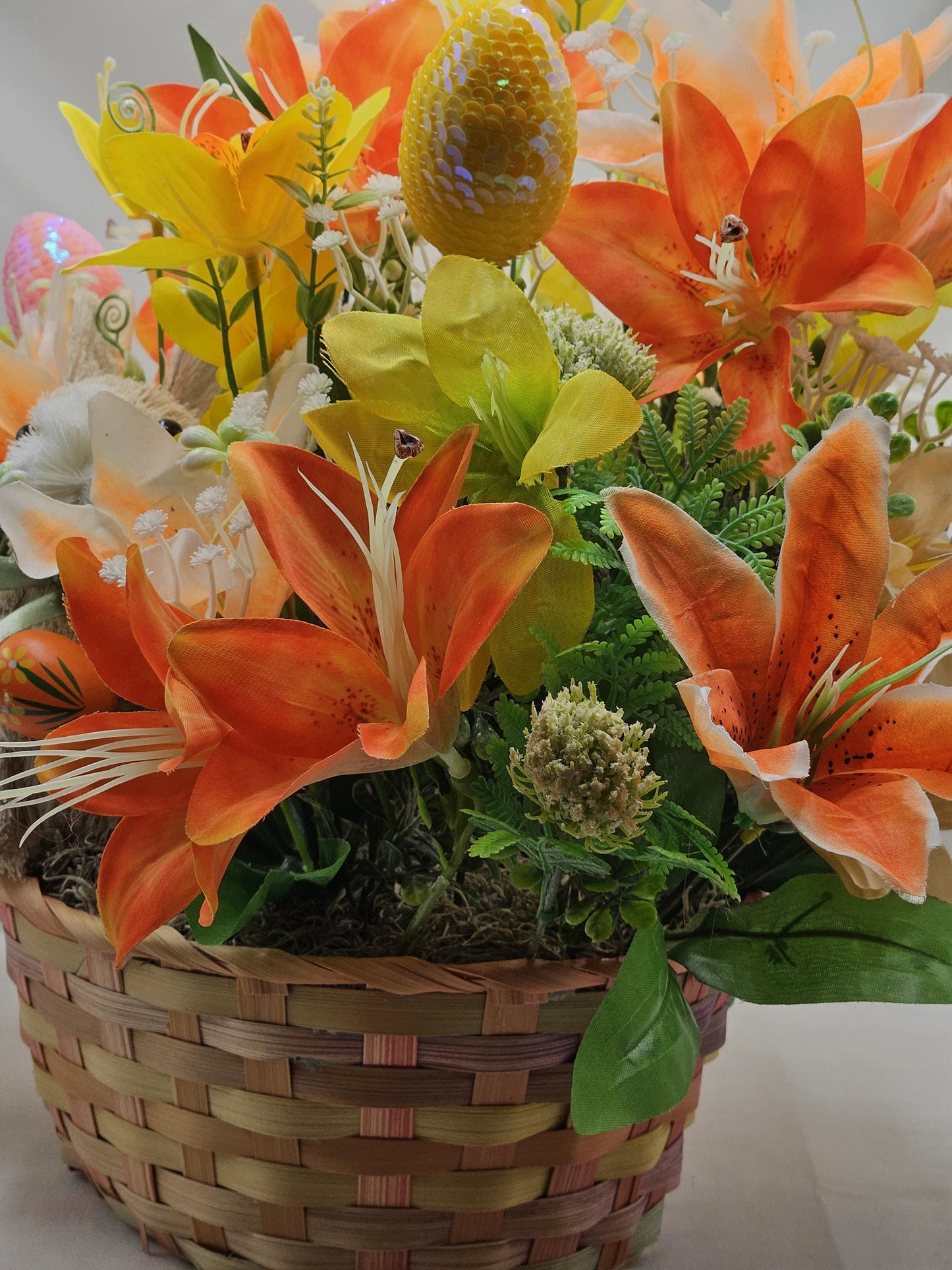 Rattan Easter Bunny in a Multi-colored Basket, Surrounded by Lush and Lovely Lilies, Greens, Baby's Breath,Orange and Yellow Hues