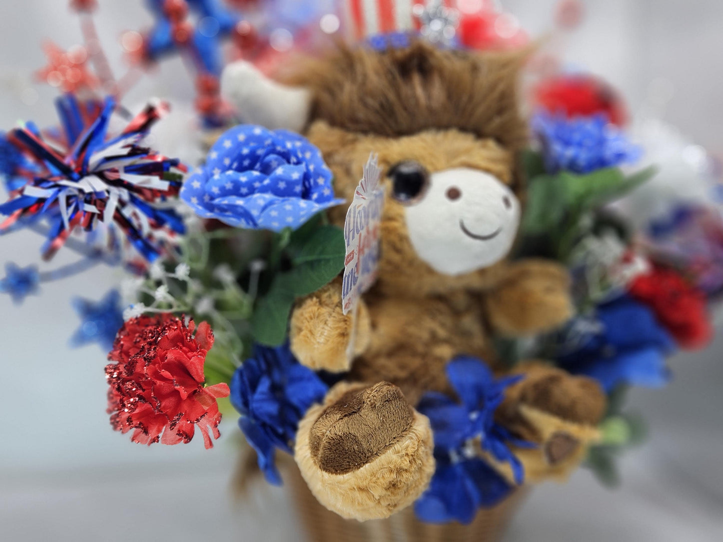 Stuffed Patriotic Steer Celebrating the USA within a Garden of Red/White/Blue Roses/Carnations/Greenery/Sparkly Stars/Other Glitter Accents