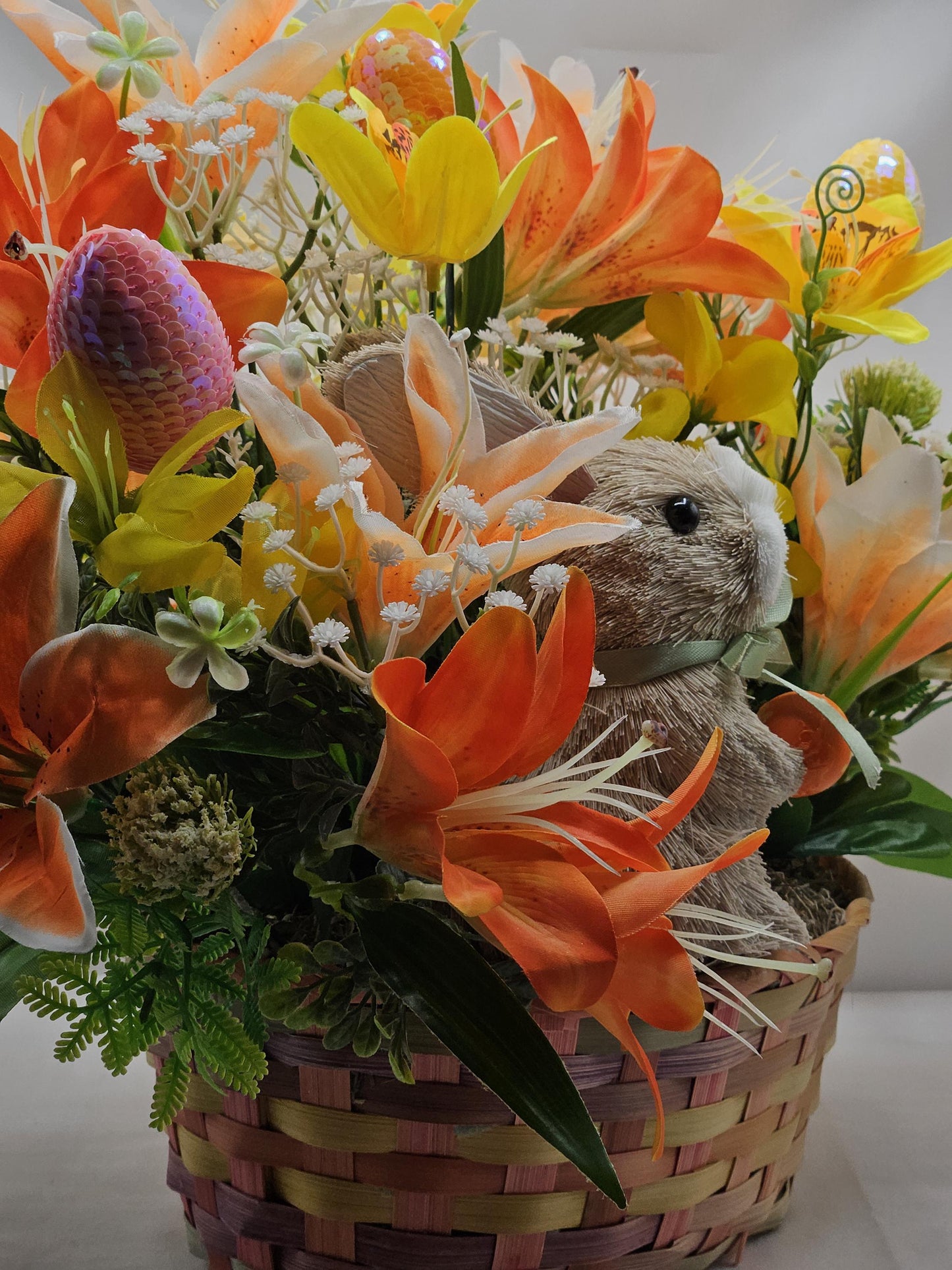 Rattan Easter Bunny in a Multi-colored Basket, Surrounded by Lush and Lovely Lilies, Greens, Baby's Breath,Orange and Yellow Hues
