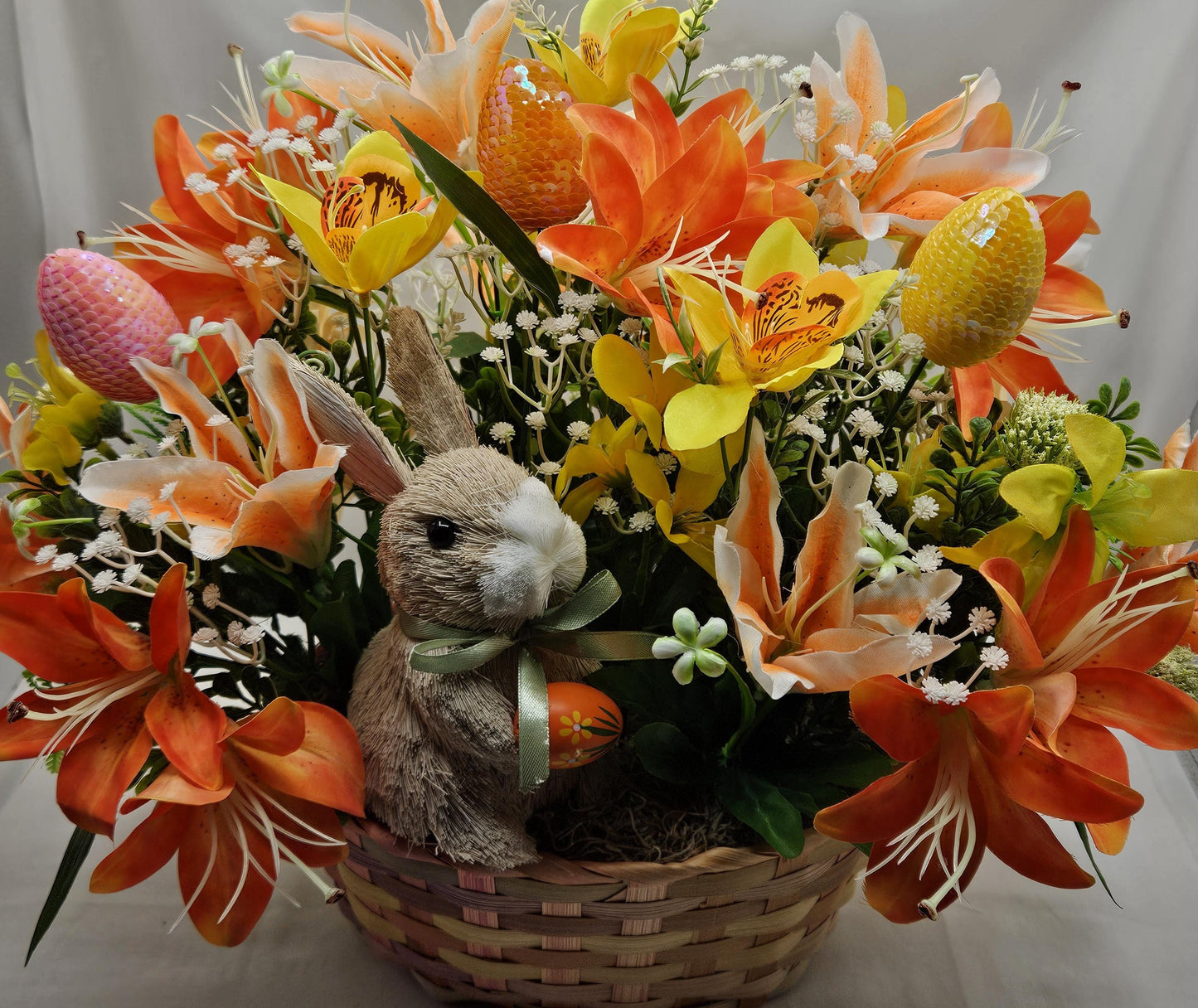 Rattan Easter Bunny in a Multi-colored Basket, Surrounded by Lush and Lovely Lilies, Greens, Baby's Breath,Orange and Yellow Hues