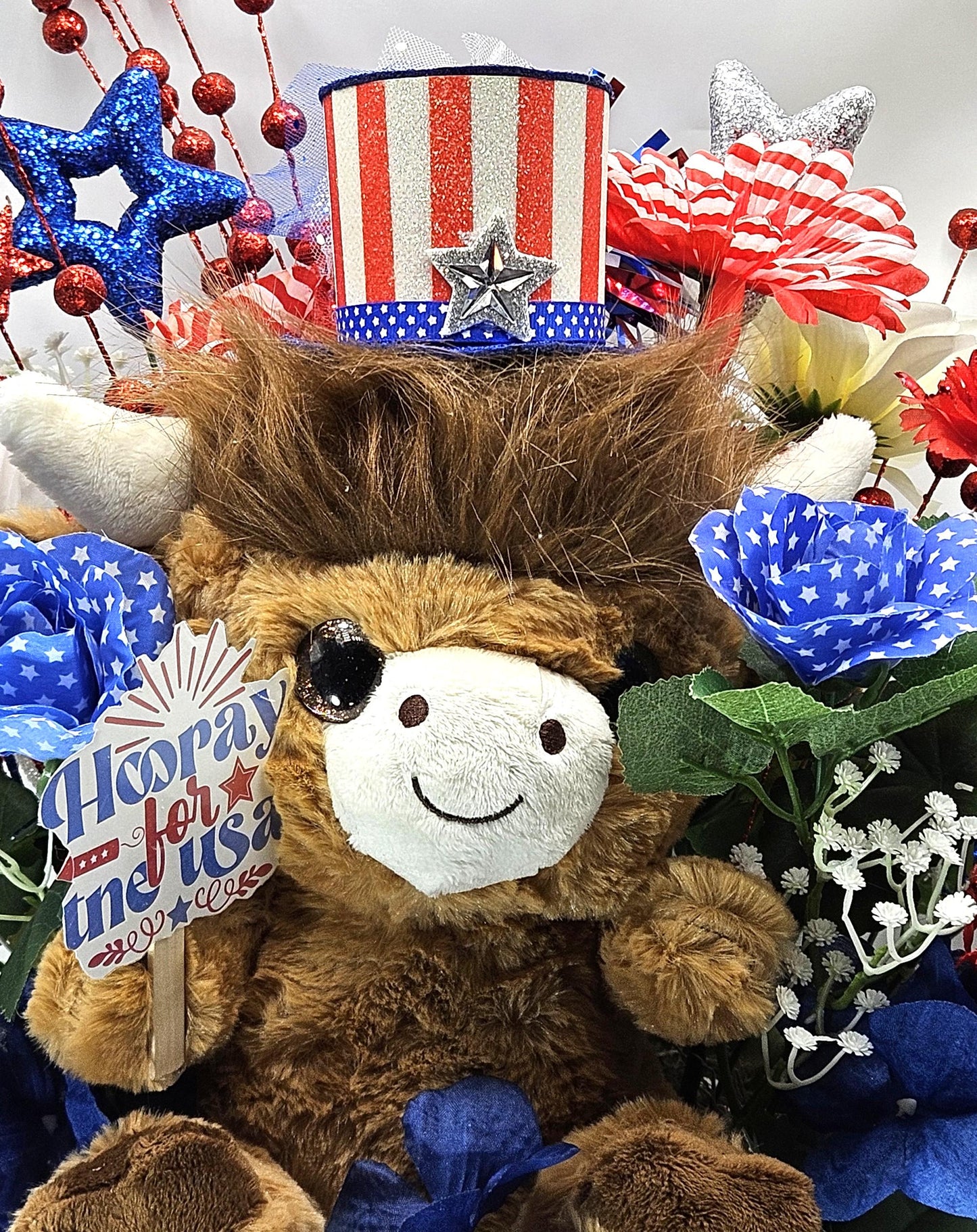 Stuffed Patriotic Steer Celebrating the USA within a Garden of Red/White/Blue Roses/Carnations/Greenery/Sparkly Stars/Other Glitter Accents