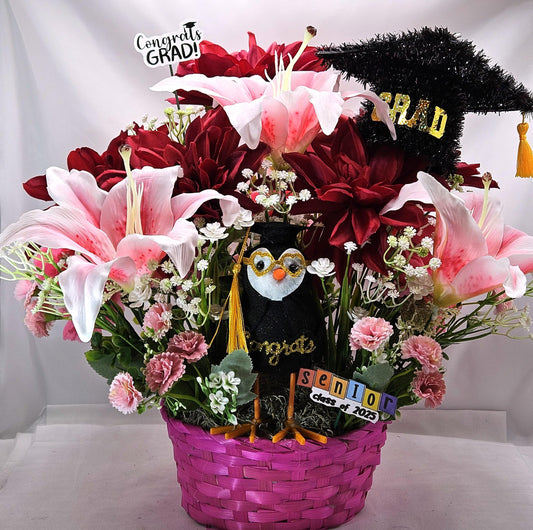 Celebrate The Graduate W/Pink Wicker Basket of Flowers/Greenery/A Sparkly Graduation Hat/A Graduate Bird In Front/Congratulations Messa