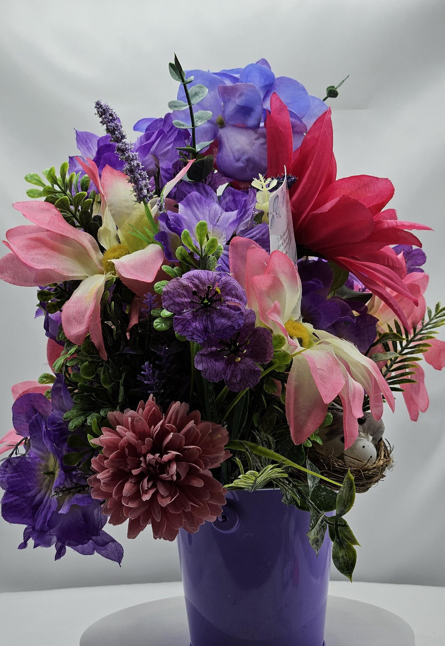 Charming Thinking Of You Bouquet set in a light purple container and accented with birds in a nest and/Atop Flowers/Pink/White/Blue/Greenery