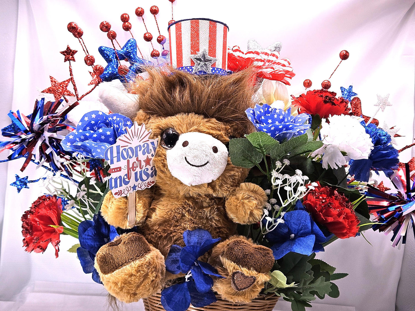 Stuffed Patriotic Steer Celebrating the USA within a Garden of Red/White/Blue Roses/Carnations/Greenery/Sparkly Stars/Other Glitter Accents